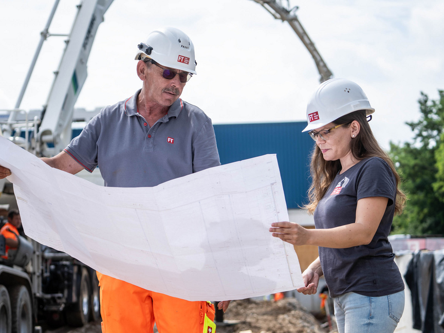 Mitarbeiter der Unternehmensgruppe Kassecker Zwei Mitarbeiter der Unternehmensgruppe Kassecker schauen gemeinsam auf einen Bauplan und stehen auf einer Baustelle.