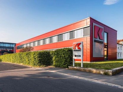 Modernes Firmengebäude von Kassecker mit roter Fassade und einem Firmenschild im Vordergrund. Der Himmel ist klar und blau.