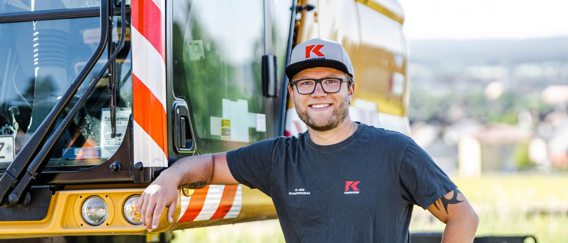 Person in Arbeitskleidung lehnt an einem Baufahrzeug.