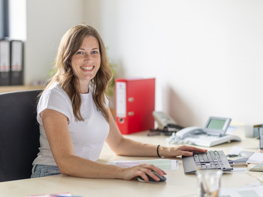 Kassecker Mitarbeiterin Buchhaltung Frau sitzt an einem Schreibtisch und hat eine Computermaus in der Hand.
