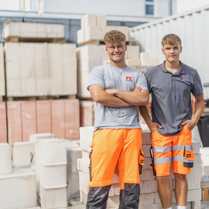 Zwei gewerbliche Auszubildende der Unternehmensgruppe Kassecker Zwei junge Männer lehnen an einem Haufen Ziegelsteinen und tragen Arbeitskleidung.