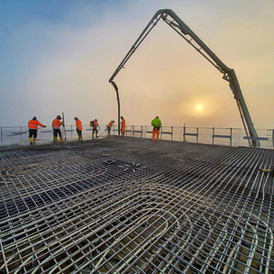 Betonpumpe auf einer Baustelle der Unternehmensgruppe Kassecker Baustelle mit Betonpumpe und Bauarbeitern bei nebligem Wetter.