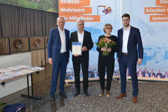 Josef Andritzky als Ehrenvorstand des VDBUM geehrt mit Urkunde steht neben drei weiteren Personen vor einer Wand.