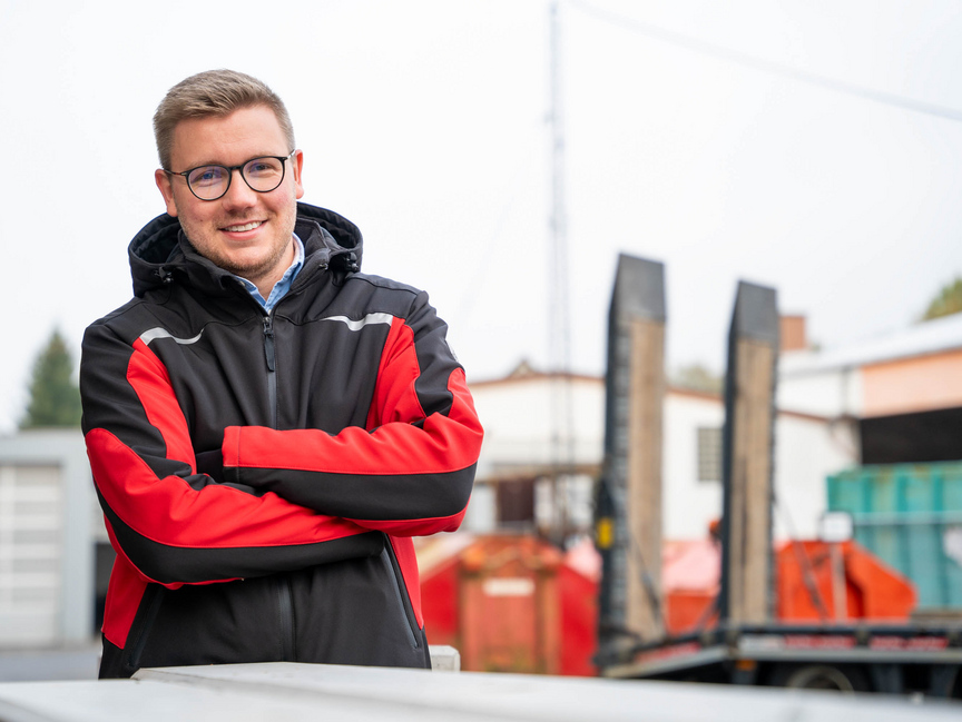 Mitarbeiter der Firma Kropf Freundlich lächelnder Mann mit Brille steht mit verschränkten Armen auf einem Bauhof.